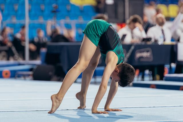 Young male gymnast bent in deep pike position on floor mat, focused and controlled, during competition.