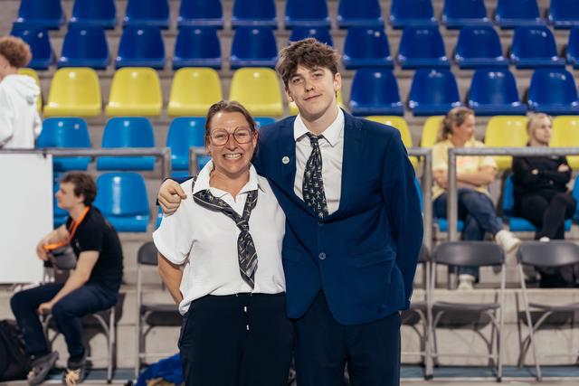 Two smiling officials in matching ties pose together in front of blue and yellow arena seating.