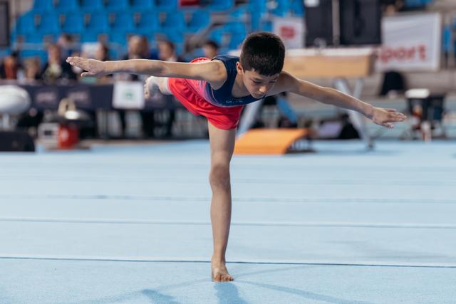 Young male gymnast performs a focused arabesque balance on the floor exercise mat at a gymnastics meet.
