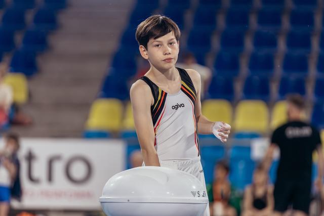 Young male gymnast chalking hands before vault attempt, looking focused and composed in a competitive arena.