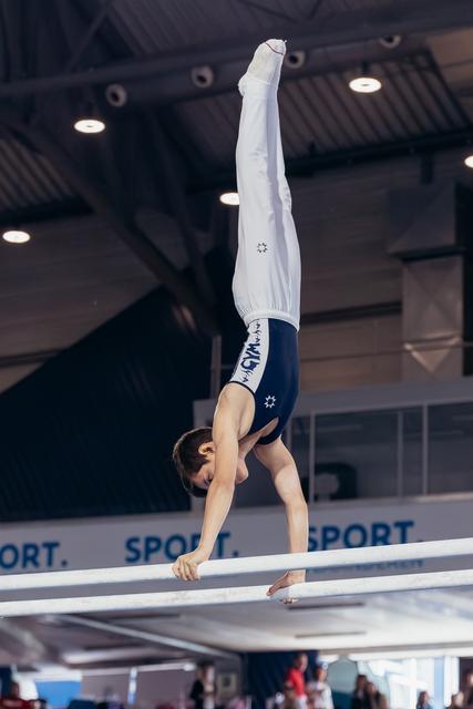 Young male gymnast performs a precise handstand on parallel bars, legs perfectly vertical, in an indoor sports hall.