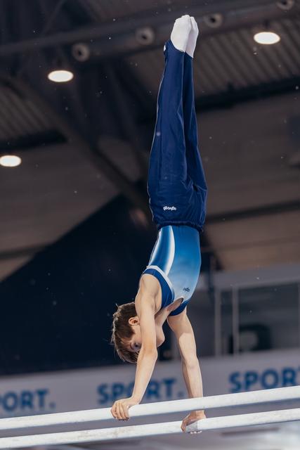Young male gymnast performs a perfect handstand on parallel bars, body fully extended, in a sports hall.