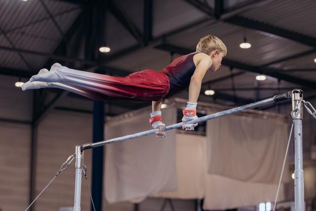 Young male gymnast holds a front lever on the horizontal bar, body fully extended, intense focus in an indoor gymnastics hall.