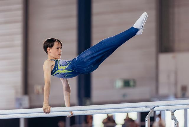 Focused young male gymnast performing a straight horizontal hold on parallel bars, legs extended, wearing blue and yellow leo.