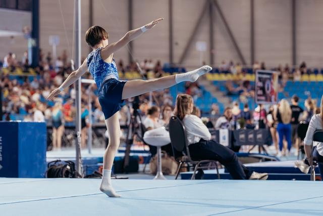 Young gymnast performs a precise arabesque on the floor exercise, arms outstretched, showing poise and concentration at a competition.