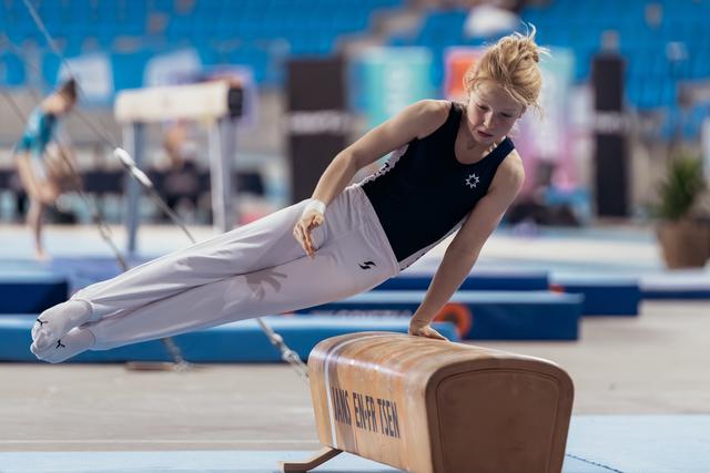 Young female gymnast performs a precise pommel horse routine, body fully extended, intense focus in a competition arena.