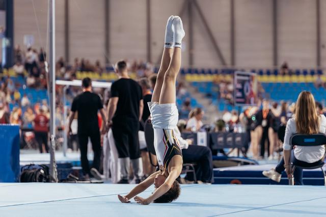 Gymnast performs a precise handstand on the floor exercise mat during a competitive gymnastics event, legs perfectly vertical.