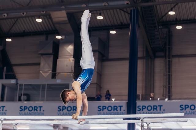 Young male gymnast performs a perfect handstand on parallel bars, body fully extended, at Sport Vlaanderen competition hall.