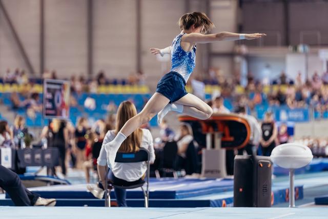 Young gymnast mid-leap on the floor exercise, arms outstretched, focused and composed during a competitive gymnastics event.