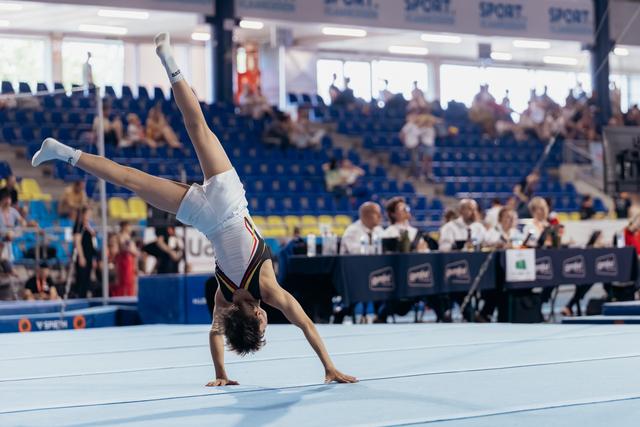 Young gymnast performs a one-handed cartwheel on the floor exercise mat during a gymnastics competition.