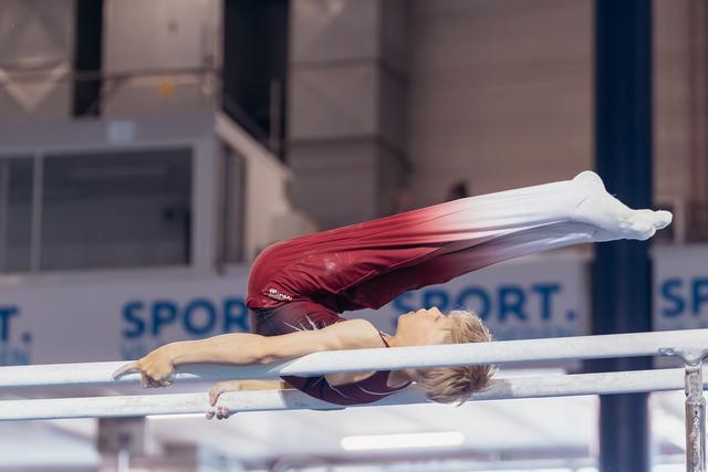 Young male gymnast performs a horizontal hold on parallel bars, body fully extended, in a sports hall.