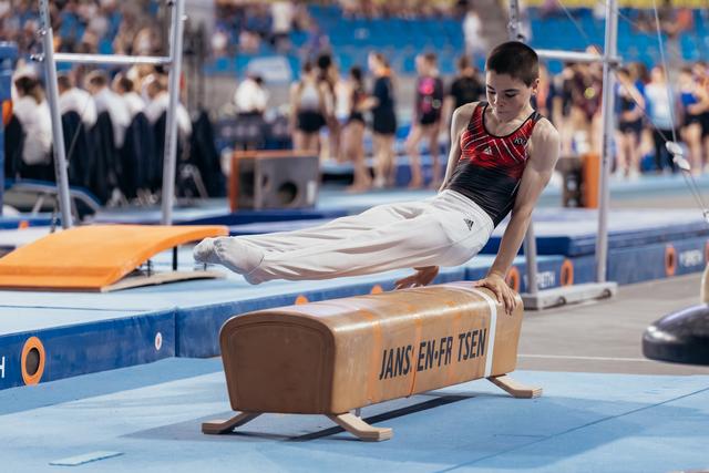 Young male gymnast holds a planche position on a pommel horse, body parallel to the floor, intense concentration.