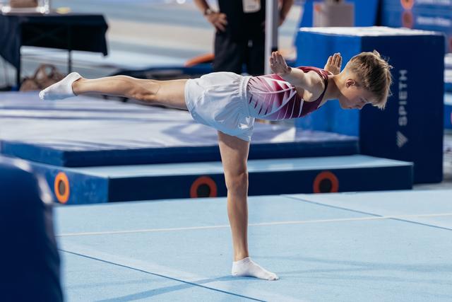 Young gymnast performs a precise arabesque on the floor, showing strong focus and body control at a gymnastics meet.