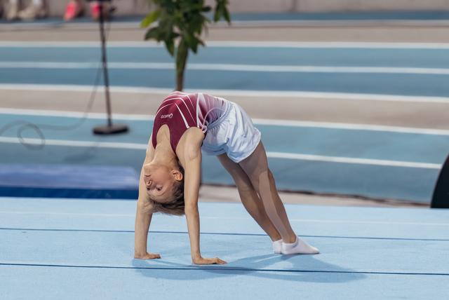 Young gymnast performs a backbend bridge on a blue gymnastics floor, focused and flexible during a sports event.