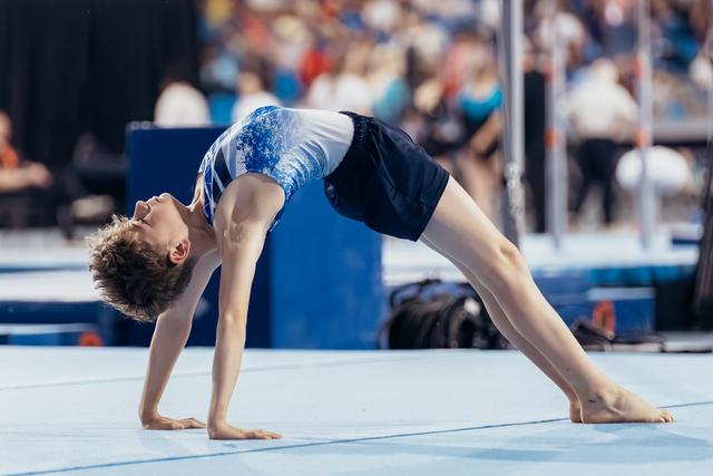 Young male gymnast performs a back bridge on the floor exercise mat, showcasing flexibility and focus during a gymnastics meet.