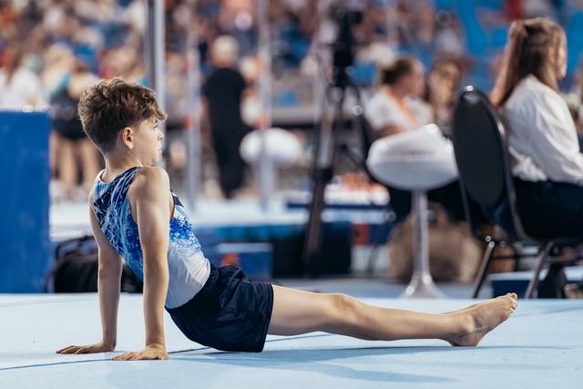 Young male gymnast performs a cobra stretch on the floor mat, focused and composed during a gymnastics meet.
