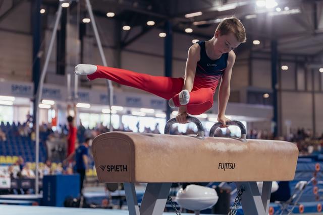 Young male gymnast performs focused pommel horse routine, legs extended, at an indoor gymnastics competition.