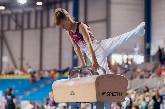 Young male gymnast concentrating intently while performing on the pommel horse at an indoor gymnastics meet.