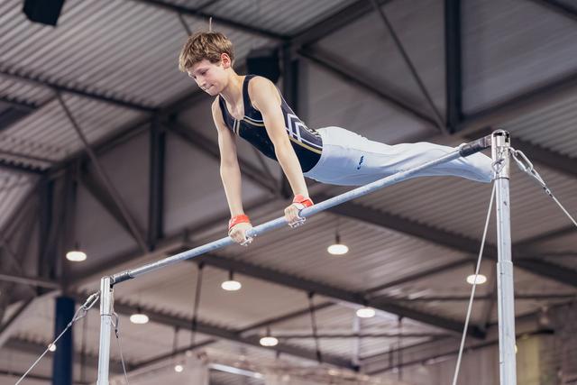 Young male gymnast performs on the horizontal bar, body horizontal, intense concentration in an indoor gymnasium.