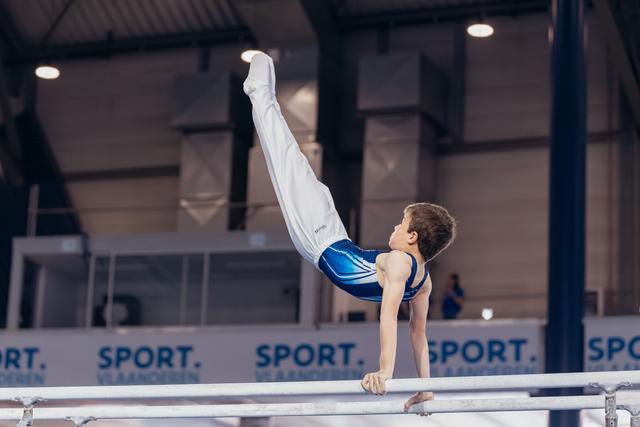 Young male gymnast performs a strong horizontal hold on parallel bars, legs raised high, at a Sport Vlaanderen event.
