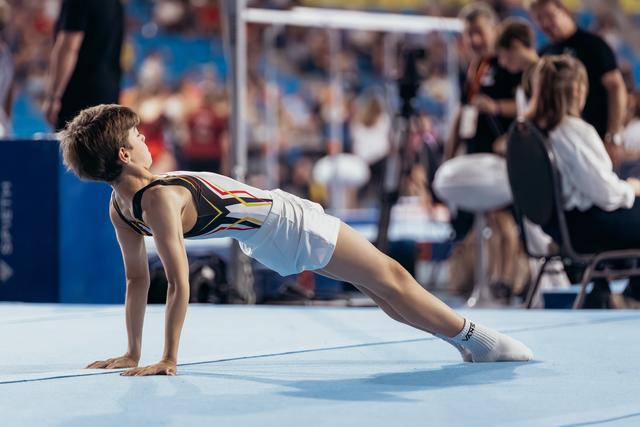 Young male gymnast holds a push-up position on the blue floor mat during a gymnastics event, focused and composed.
