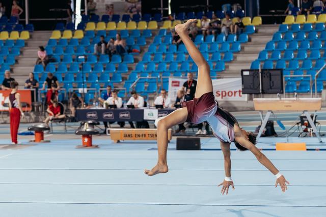 Young male gymnast executes a dynamic airborne back walkover on the floor exercise mat during a gymnastics competition.