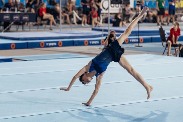 Young gymnast performing a cartwheel on the floor exercise mat, body fully extended, competing at a gymnastics event.