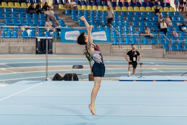 Young male gymnast lands with arms raised triumphantly on the floor exercise mat during a gymnastics meet.