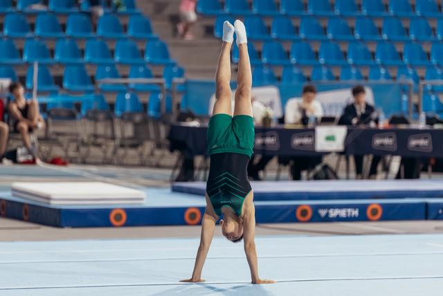 Young gymnast performs a perfect handstand on floor exercise, legs stretched upward, wearing a green leotard at a competition.
