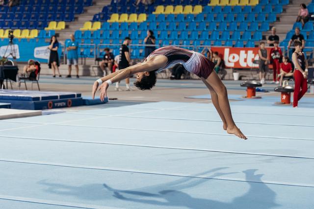 Young gymnast performs a powerful backflip on the floor exercise mat, body arched gracefully mid-air during competition.