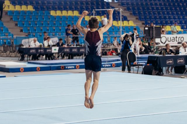 Young male gymnast raises fists overhead in triumph on the floor exercise mat during an indoor gymnastics meet.