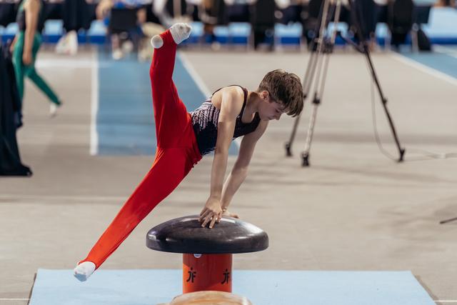Young male gymnast in red leotard executes a dynamic vault, body extended, intense focus during competition.