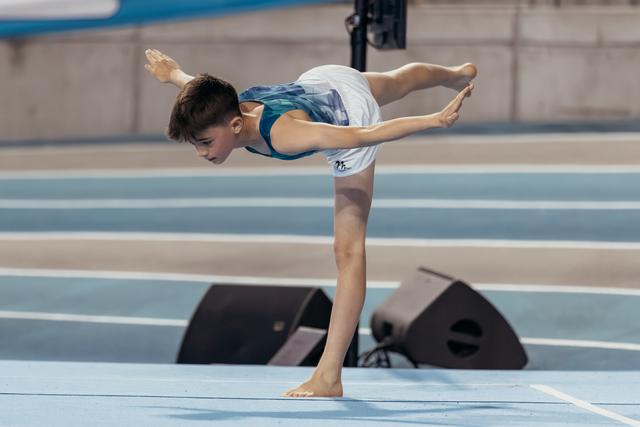 Young male gymnast performs a focused arabesque balance on the floor exercise mat during a competition.