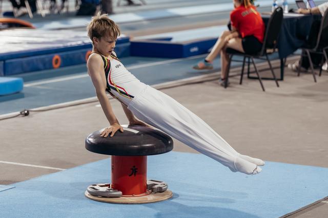 Young male gymnast concentrating intensely while performing a support hold on a mushroom apparatus during a competition.