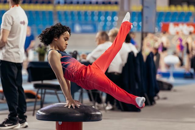 Young gymnast performs a focused straddle hold on a mushroom apparatus during a gymnastics event.
