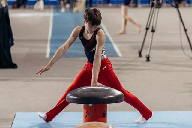 Young male gymnast performs a straddle vault, leaning forward with intense focus during a gymnastics competition.