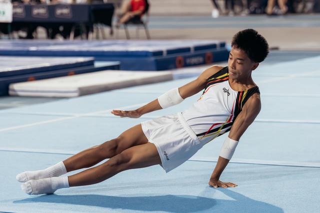 Young male gymnast lands on the floor mat, balancing with one hand, showing focus and composure during his routine.