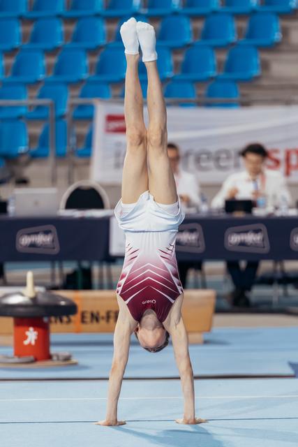 Young gymnast performing a perfect handstand on the floor exercise mat during a gymnastics competition.