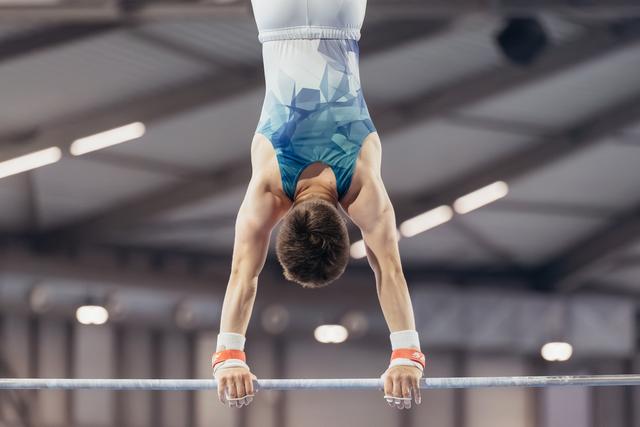Young male gymnast holding an inverted handstand on the high bar, showing strength and control in an indoor gymnasium.