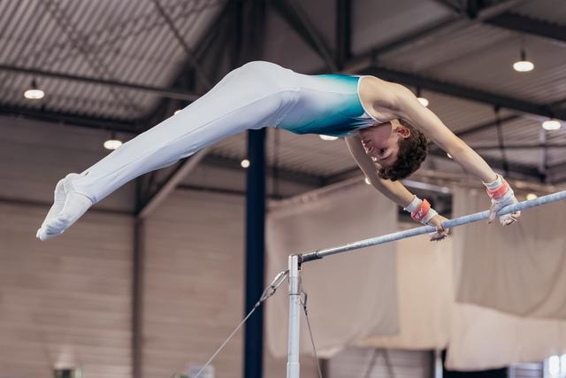 Young gymnast performs a pike hold on horizontal bar, body perfectly parallel, intense focus in an indoor gymnasium.