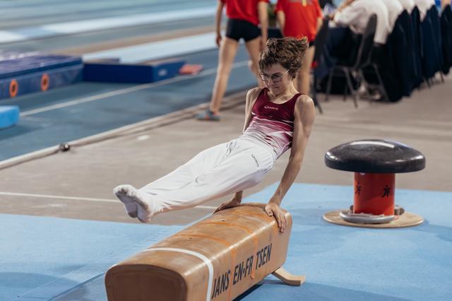 Young gymnast with glasses performs a straddle hold on the pommel horse, concentrating intensely during competition.