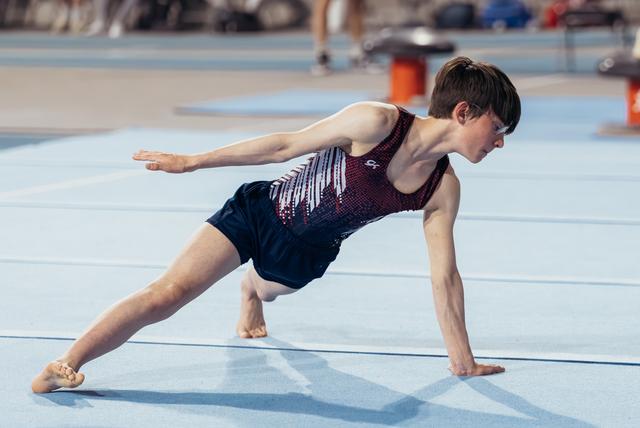 Young male gymnast performing a dynamic floor exercise pose, one hand planted, arm extended, intense focus on his face.
