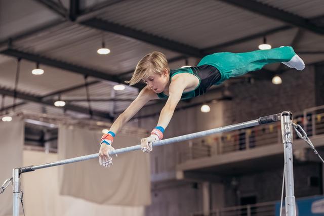 Young male gymnast performs a horizontal bar routine, body fully extended parallel to bar, intense focus, indoor gym.