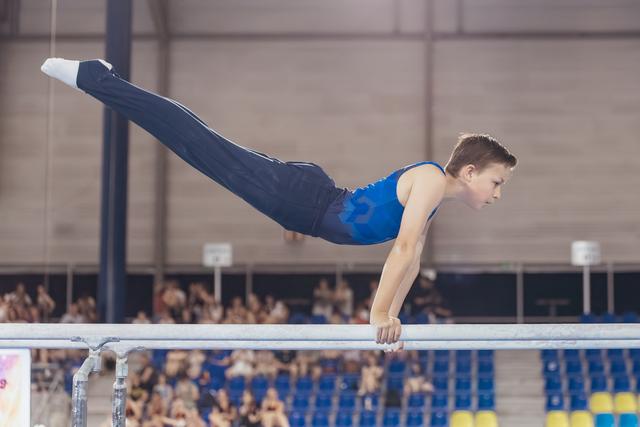 Young male gymnast holds a perfect planche on parallel bars, body fully horizontal, expression intense with concentration.
