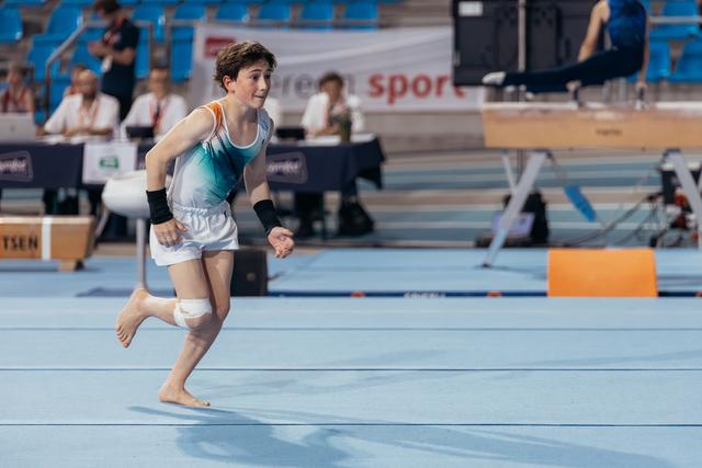 Young male gymnast sprints barefoot across the blue floor, focused and determined, during a gymnastics competition.