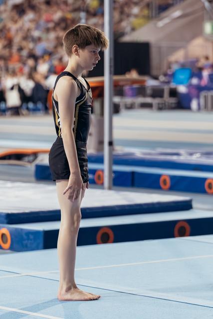 Young male gymnast stands barefoot on the floor mat, expression serious and concentrated, preparing for his routine.