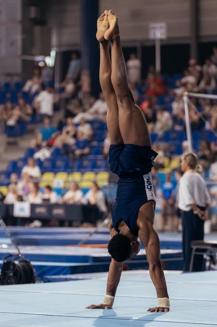 Male gymnast performs a perfect handstand on floor exercise, body fully extended, competing before a live audience.