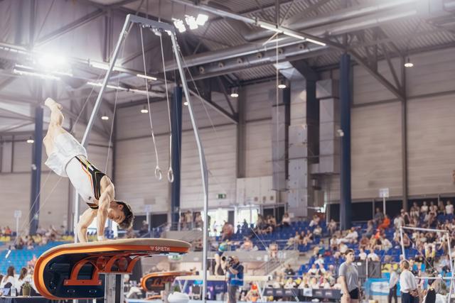 Male gymnast performs an inverted handstand on a Spieth vault during a packed indoor gymnastics competition.