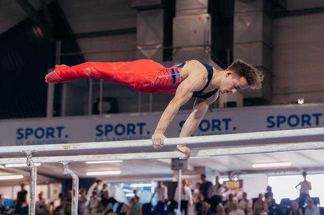 Male gymnast holds a perfect planche on parallel bars, body fully horizontal, intense concentration on his face.