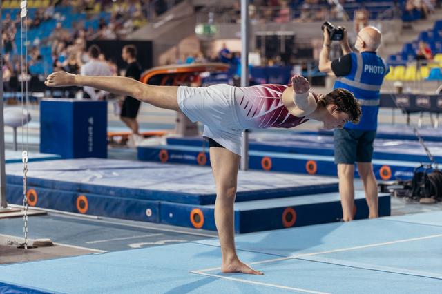 Young gymnast holds a precise arabesque on the floor, focused and controlled, at an indoor gymnastics competition.